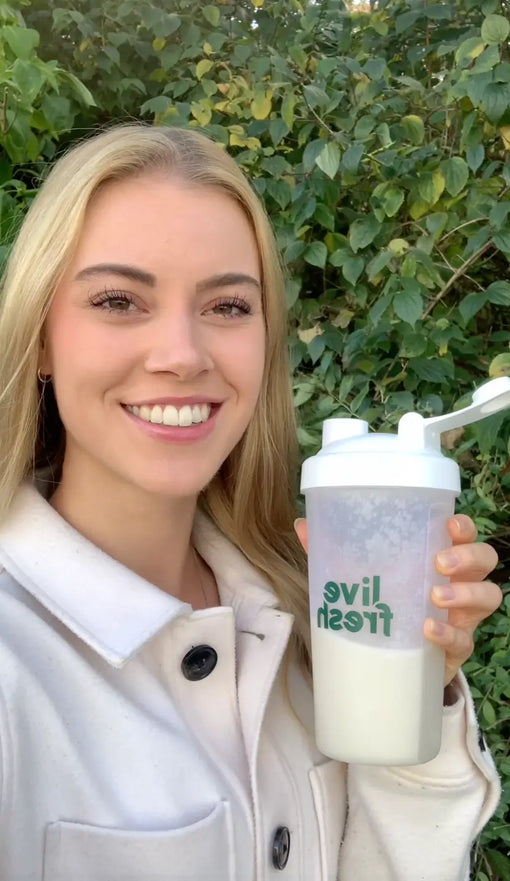 Foto einer jungen Frau wie sie mit einem Schönen Stilglas der Kamera zuprostet und dabei lächelt