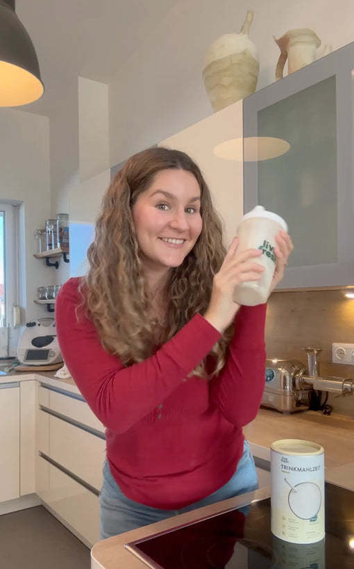 Frau mit lan gen dunklen Haaren schaut in die kamera, vor ihr steht ein aufgeklappter Laptop.
