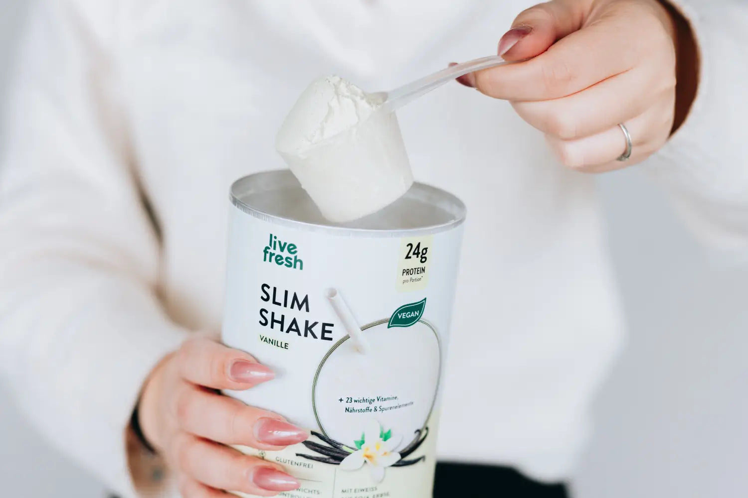 Messlöffel mit Slim by LiveFresh Vanille Pulver wird aus der Dose mit 24g Protein und veganem Siegel entnommen.